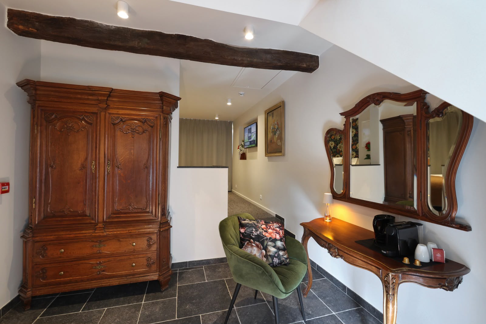 L'Ambre : coin salon avec armoire ancienne en chêne sculpté, fauteuil de velours vert et console à miroir